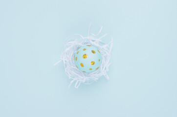 Fashion easter background - blue egg with golden dots in white nest on blue color, top view.
