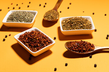 Collection of three spices on wooden spoons and white bowls on orange background,top view.Flat lay