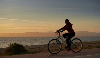 Fototapeta na wymiar Woman in sports suit, rides a bicycle, in front of the sea, at sunset