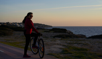 Fototapeta premium Woman in sports outfit contemplates the sea leaning on her bicycle