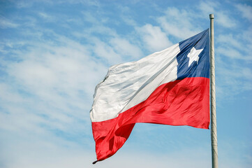 Fototapeta na wymiar Big chilean flag waving in front of blue sky with copy space. Chile country flag on pole for identity and patriotism concept. Nation and state emblem, politics and union.