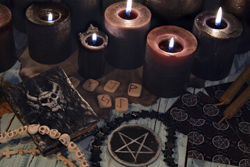 Still life with runes, black candles, diabolic witch book, tarot cards and pentagram.