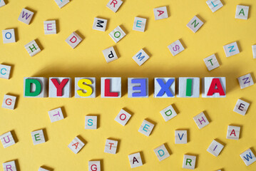 wooden alphabet blocks with DYSLEXIA word in the center on yellow background. Concept of Dyslexia awareness and human brain development