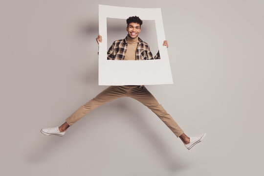 Full size photo of dark skin handsome man jump wear casual clothes hold frame isolated on grey color background