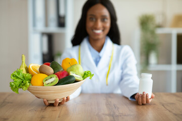 Happy black dietitian offering choice between fresh products and tablets at clinic