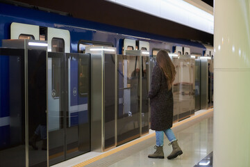 A full-length photo of a woman in a medical face mask to avoid the spread of coronavirus who is going to the modern subway car. A girl in a surgical mask is keeping social distance on a metro station.