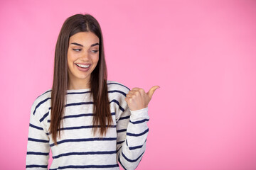 Beautiful woman wearing casual t-shirt standing over isolated pink background smiling and looking at the camera pointing with two hands and fingers to the side