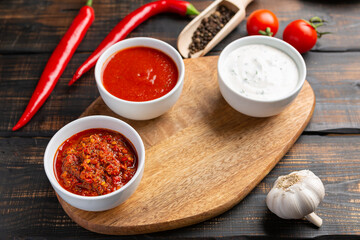Different types of sauces in bowls on a cutting Board with garlic. On dark rustic background