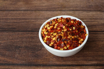 Chilli Flakes in bowl on wooden texture, close up shot