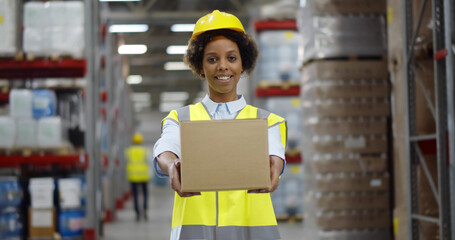 Afro-american female warehouse worker with large box posing at camera