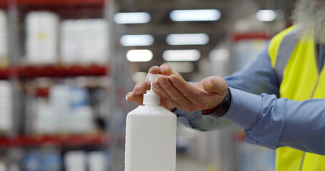 Cropped shot of industrial worker using sanitizer disinfecting hands in warehouse