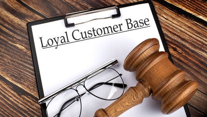 Paper with LOYAL CUSTOMER BASE with gavel, pen and glasses on the wooden background