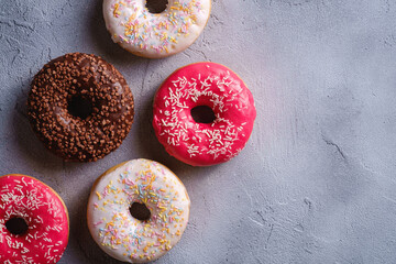 Chocolate, pink and vanilla donuts with sprinkles, sweet glazed dessert food on concrete textured background, top view copy space