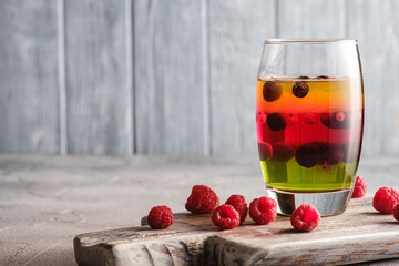 Jelly dessert with berries in glass on old wooden cutting board, sweet colorful layered pudding,...