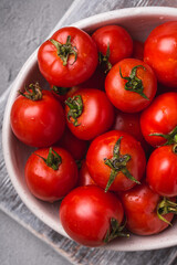 Fresh ripe tomatoes with water drops in bowl on old wooden cutting board, stone concrete background, top view macro