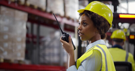 Afro-American female worker of warehouse reporting through walkie-talkie - obrazy, fototapety, plakaty