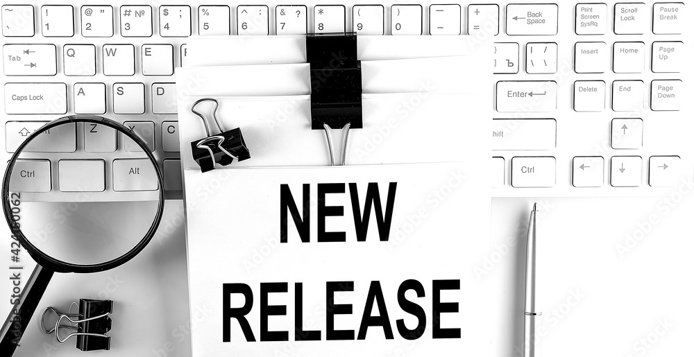 Poster words new release written on papers on a computer keyboard with magnifier and pen