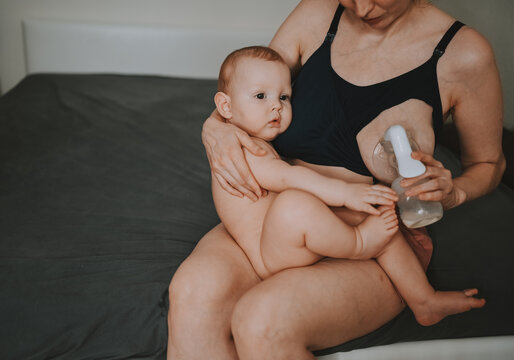 Young Mother With Newborn Cute Infant Naked Baby Boy, Holding Him On Arms, Using Breast Pump Hugging And Breastfeeds With Breast Milk. Healthy Child, Concept Of Hospital And Happy Motherhood. Nursery.