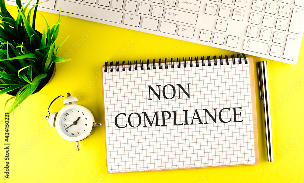 Aufkleber non compliance text on notebook with keyboard , pen and alarm clock