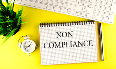 NON COMPLIANCE text on notebook with keyboard , pen and alarm clock