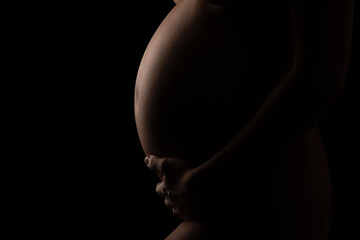 Pregnant girl in the dark, low key. Black background.