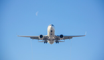 the airliner with landing gear lands against the background of the off runway lights against the background of a clear sky and against the moon during the day 