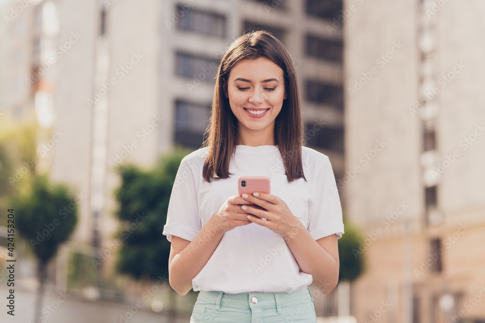 Sticker Photo of optimistic brunette lady look telephone wear white t-shirt walking in park outside