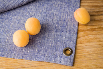 three ripe yellow apricots lie on lilac linen napkin.