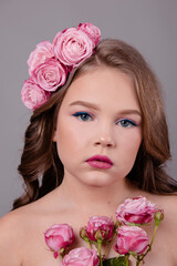 brunette teenage girl with pink roses in her hair on gray background. flowers in curls on the head. fashion photo