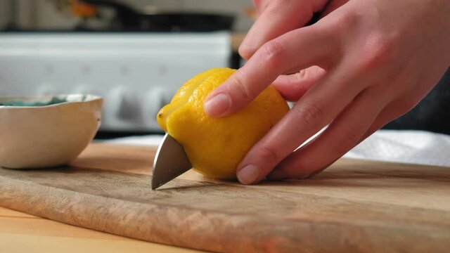 Сhef cuts yellow lemon in the kitchen on a wooden board. Female hands in a light kitchen cut a yellow lemon on the board. Сlose-up in slow motion, colorful