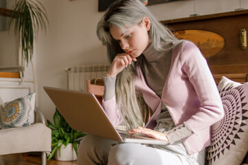 A casually dressed young woman is doing freelance work, on the laptop, from her home decorated in vintage style.