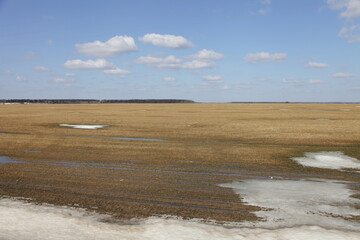 Beautiful vast brown ploughed field with snow against a blue sky on a Sunny spring day — land...