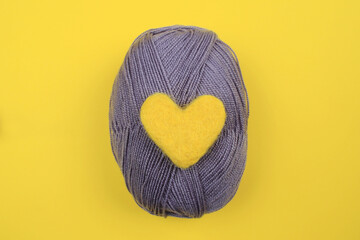A yellow wool heart rests on a gray ball of knitting thread.The concept of handwork, needlework and needlework.The colors of 2021 are gray and yellow. Top view.Flat styling style