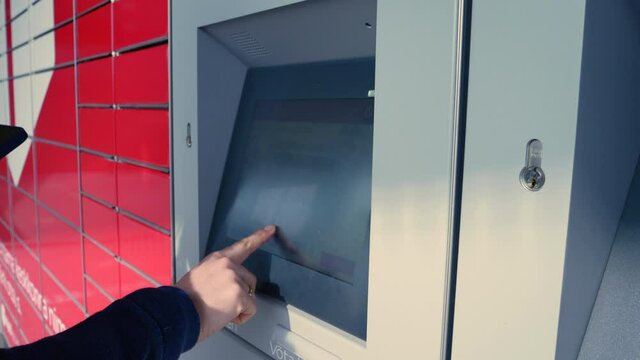 A man using an automated self-service post terminal machine or locker to receive a parcel. Using fingers on a touchscreen interface at a self-service machine to purchase postage to send parcels