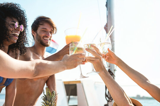 Happy multiracial friends cheering with tropical cocktails at boat party - Young people having fun in sea tour - Travel and summer vacation concept - Focus on close-up hands