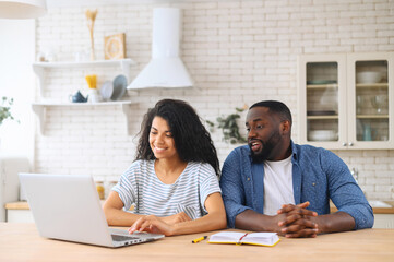 Modern young African American couple attentively watching online video classes or blog, sitting in...