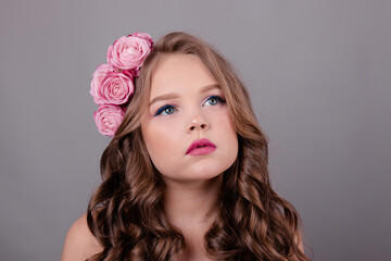 brunette teenage girl with pink roses in her hair on gray background. flowers in curls on the head. fashion photo