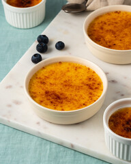 Creme brulee. Side view of French vanilla cream dessert. Spanish crema catalana, burned cream, burnt or Trinity creme. Four white ramekin with caramelized sugar on table. Side view, vertical
