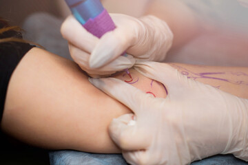 Master tattoo draws the red paint on the clients tattoo. Tattoo artist holding a pink tattoo...