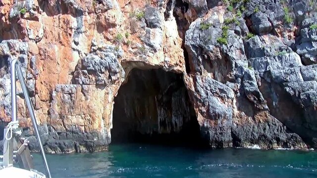 Boat going to enter a large cave in the jagged cliff along Marina di Camerota coastline, Italy.