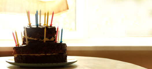 silhouette of a chocolate cake with unlit candles on the background of a window on a sunny day. we will celebrate birthday in the evening
