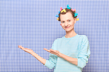 Happy girl with bright hair curlers on head is pointing at copy space