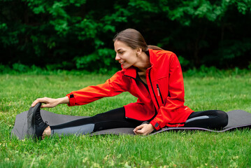 girl in the park sitting on a yoga mat doing stretching