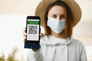 A defocused young girl is holding a passport and a smart phone with a certificate of vaccination against the Covid-19 disease. focus on the smart phone. Health Passport concept