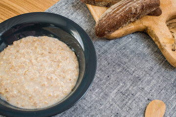 plate of oatmeal and sliced rye bread lie on wooden table