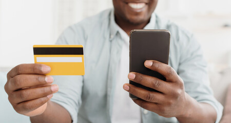 Online payment. Unrecognizable black buyer holding credit card and using smartphone for shopping at home