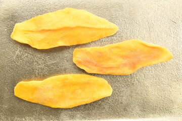 Three light yellow dry mango slices on a metal tray, close-up, top view.