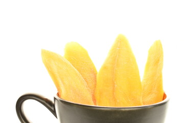 Several light yellow slices of dry mango with a black cup, close-up, isolated on white.