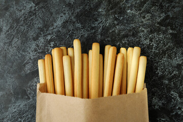 Paper bag with grissini breadsticks on black smoky background