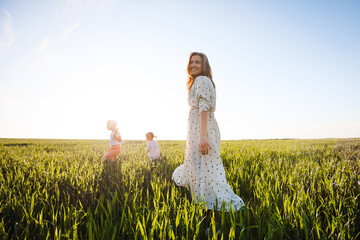A mother with two daughters is walking in a green field. Hugs and feelings.